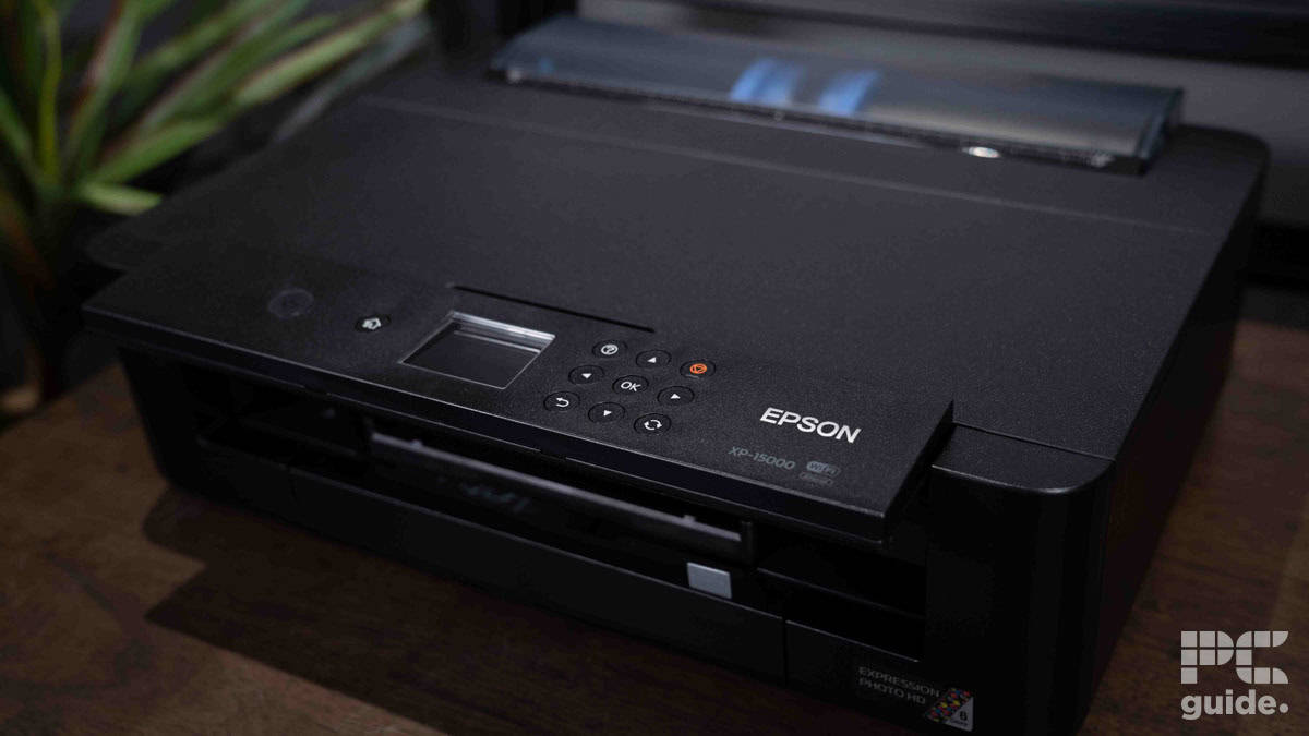 An Epson Expression XP-15000 wide-format printer on a wooden desk, with part of a green plant visible to the left.