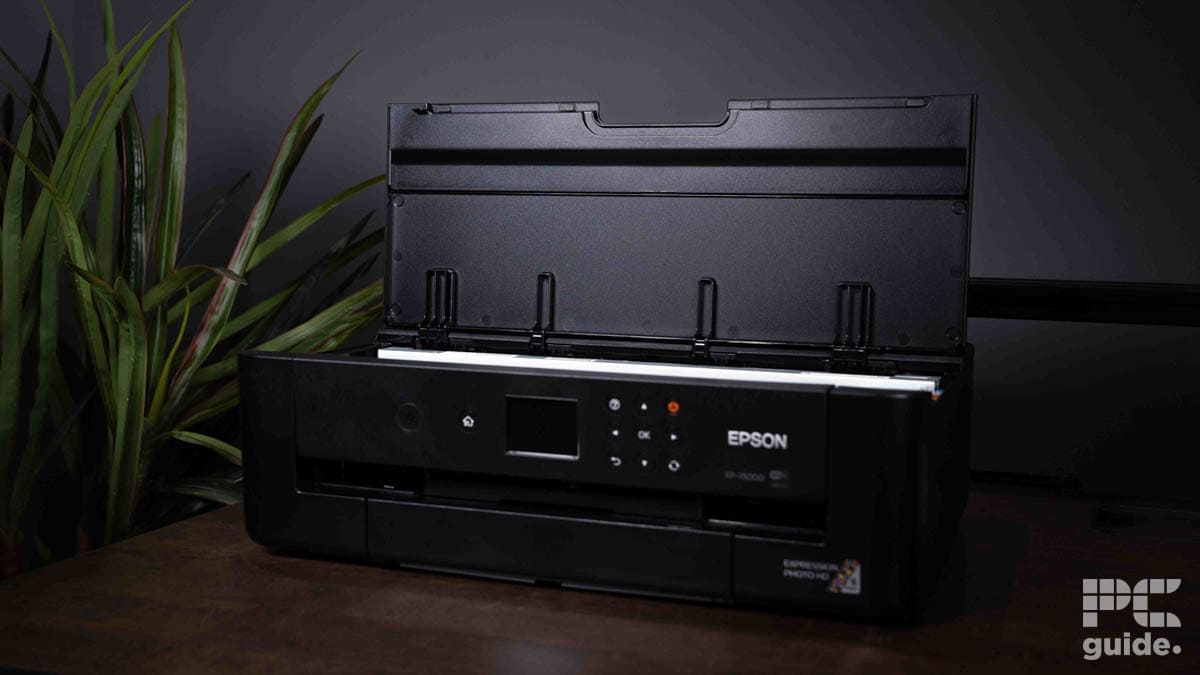 A black Epson Expression XP-15000 portable printer on a wooden desk with a green plant in the background.