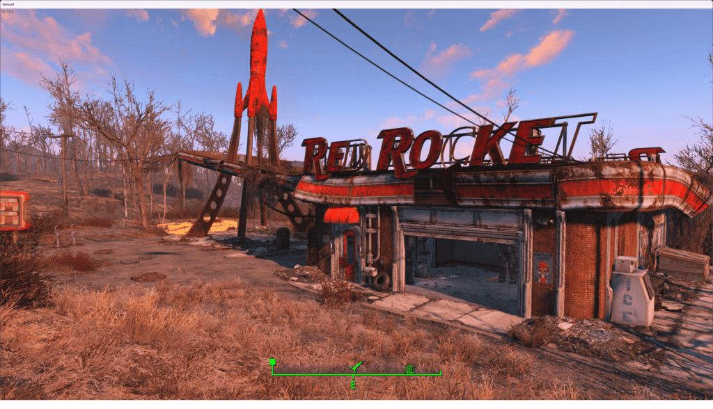 A desolate scene showing an abandoned red rocket gas station in a Fallout 4 post-apocalyptic landscape with scattered debris and dry grass.