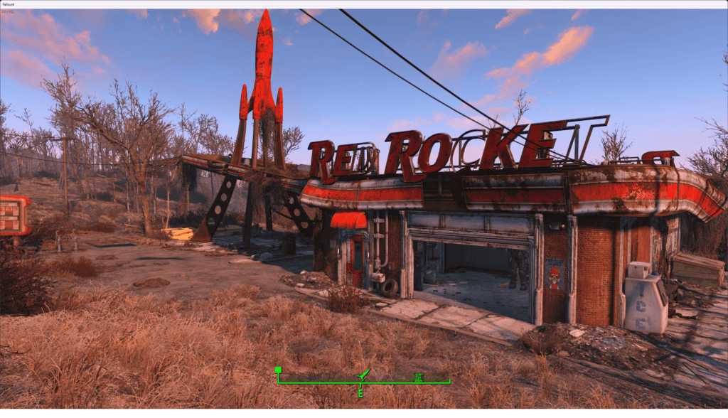 An image depicting the red rocket gas station in a desolate, Fallout 4 setting, characterized by barren landscape and decayed structures under a clear sky.