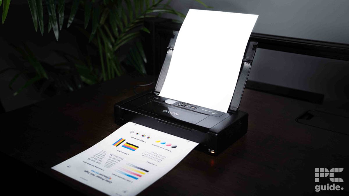 A black Epson WorkForce WF-110 sits compactly on a desk, printing a colorful document with charts and graphs despite its slow printing speed.